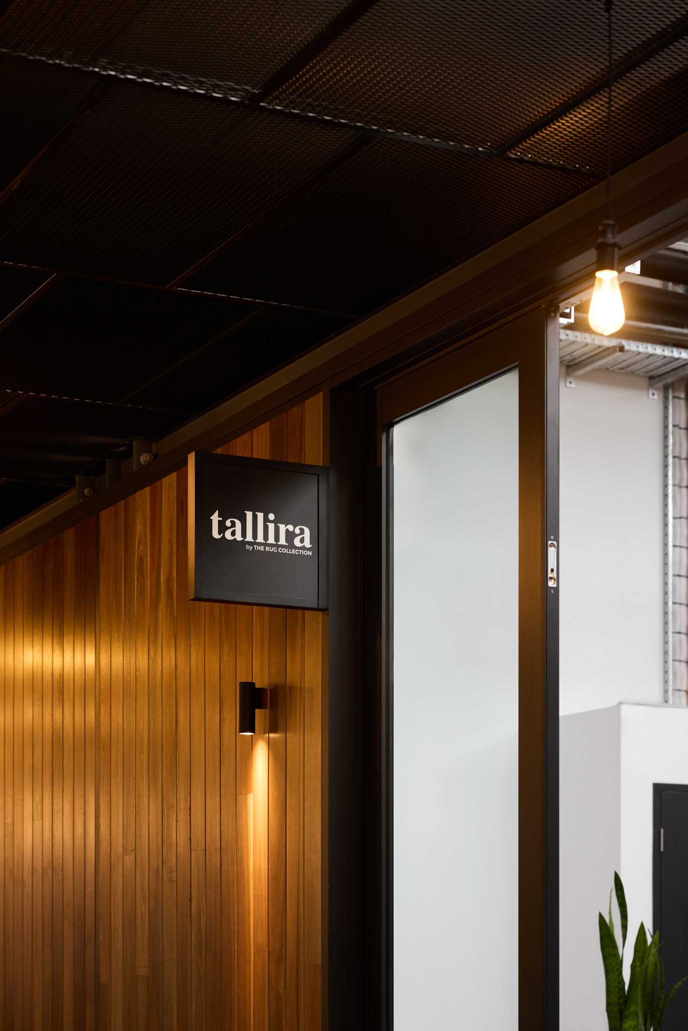 Luma Developments A wooden wall with a "tallira" sign and a glass door is illuminated by a single bulb hanging from the dark ceiling.