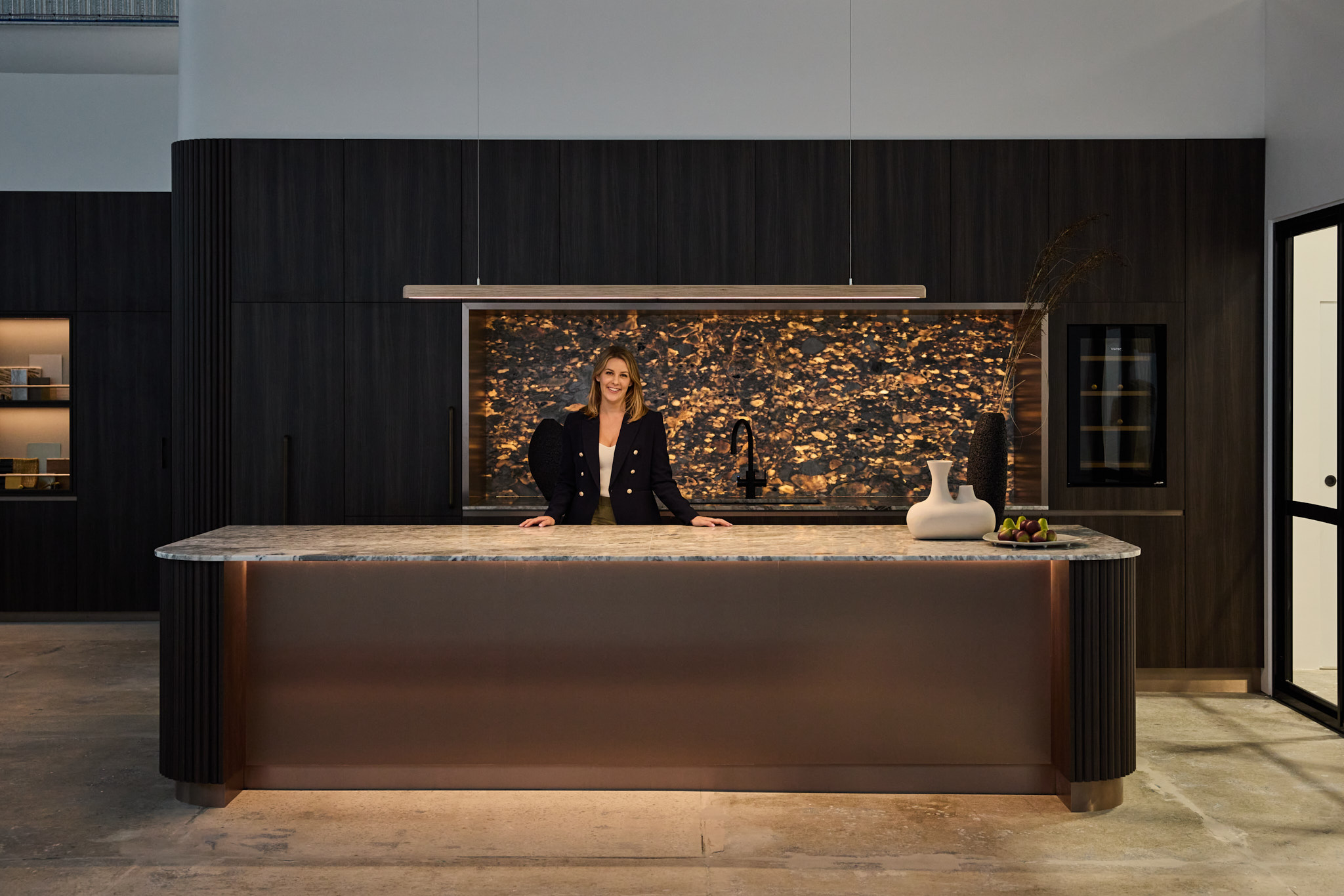 Luma Developments A modern kitchen island with dark cabinetry, a marble countertop, and a decorative vase highlights the well-lit room's interior design.