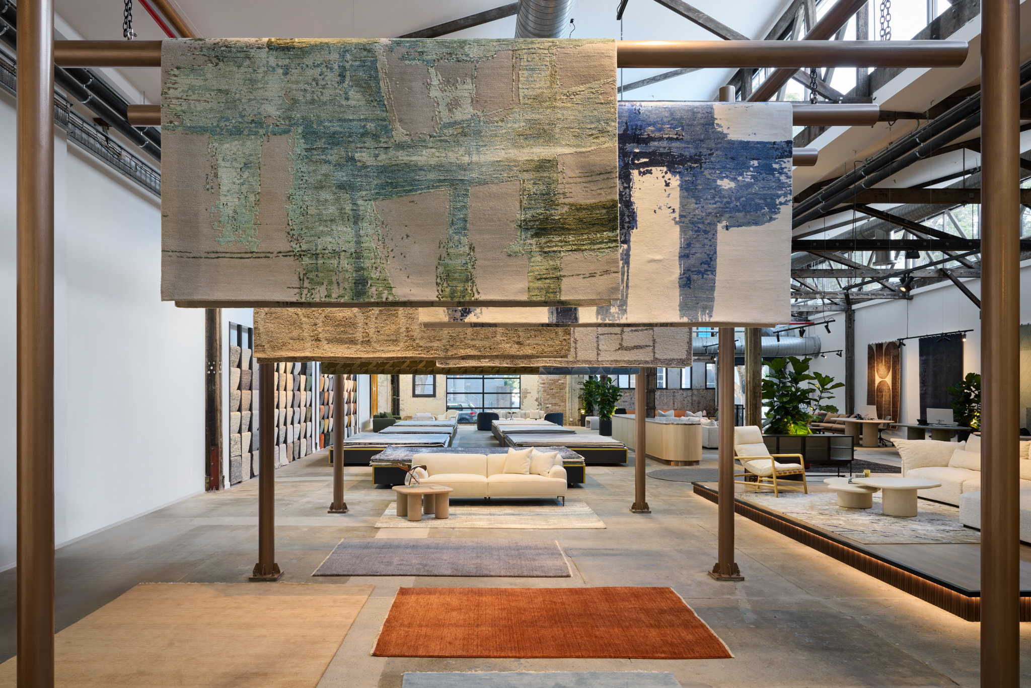 Luma Developments A contemporary showroom features hanging rugs, seating areas, and decorative plants beneath industrial-style beams.